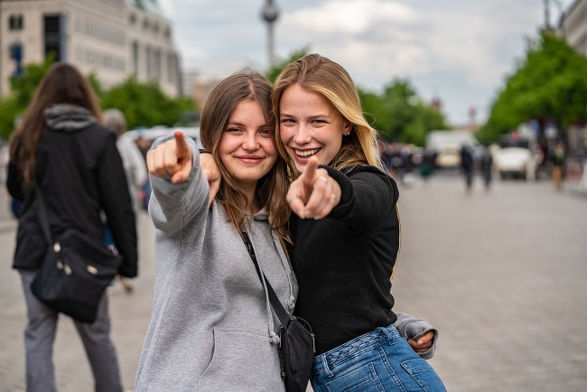 Klassenfahrt in Berlin - Zwei Schülerinnen zeigen Richtung Kamera. Im Hintergrund ist der Berliner Fernsehturm zu sehen.