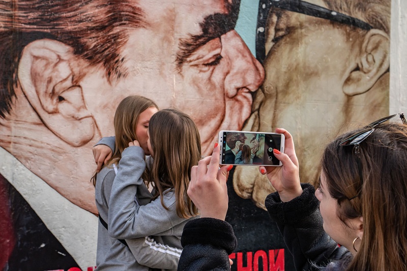 Zwei Schülerinnen machen den Bruderkuss vor der East Side Gallery in Berlin.