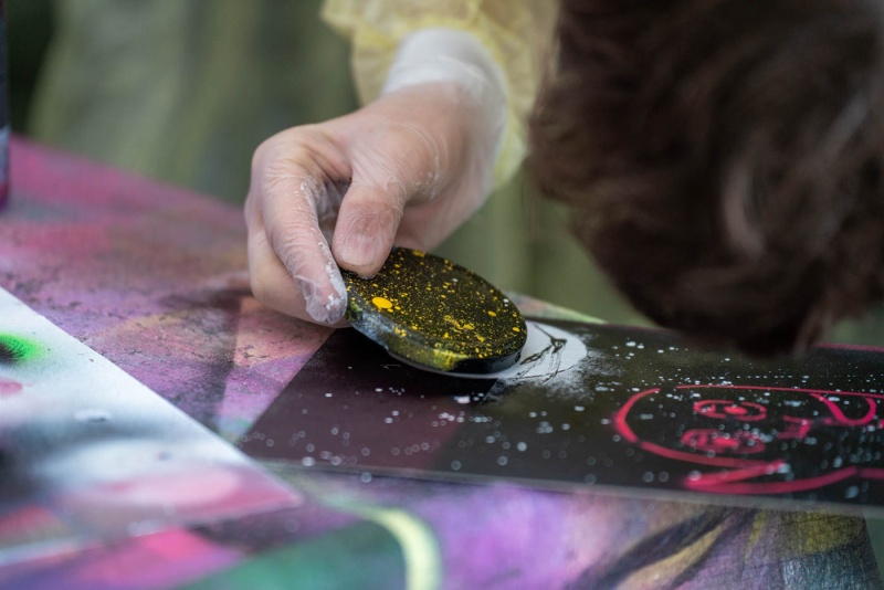 Mit Schablone wird Stencil-Art auf Graukarton gesprüht.