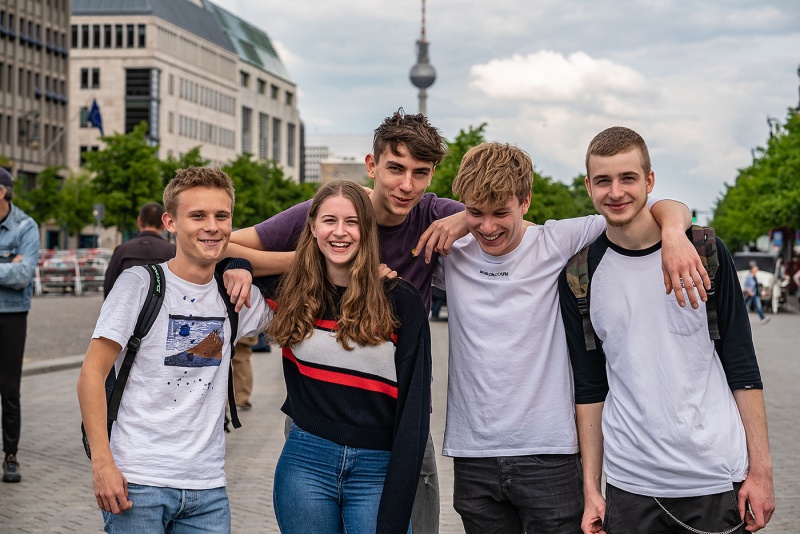 Klassenfahrt nach Berlin - fünf Schüler*innen lachend auf dem Pariser Platz, im Hintergrund sieht man den Fernsehturm.